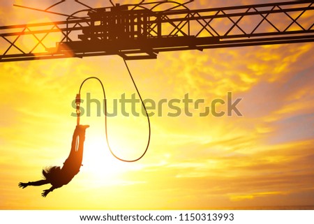 Silhouette of women jumping down bungee jump sport in sunset and light flare