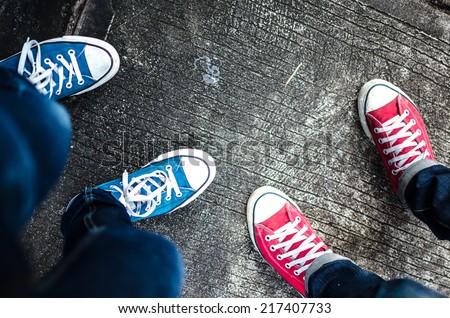 Red and Blue Sneakers shoes walking on Dirty concrete top view , Canvas shoes walking on concrete , two sneakers behind each others as a sign of love , Sneakers shoes Couple