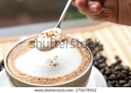 Cup of coffee with foam being stirred by a woman, handCappuccino stirred ,Coffee stirred