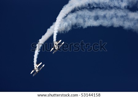 Two aerobatic airplanes approaching with white smoke trail