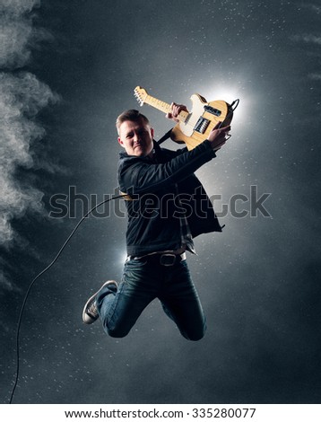Rock and Roll Guitarist jumping with electric guitar with smoke and powder in background