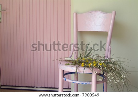 old pink chair and flowers in front of green wall and pink door.