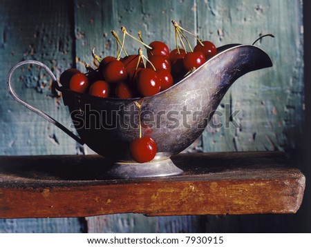 cherries in a silver gravy boat on a wooden shelf