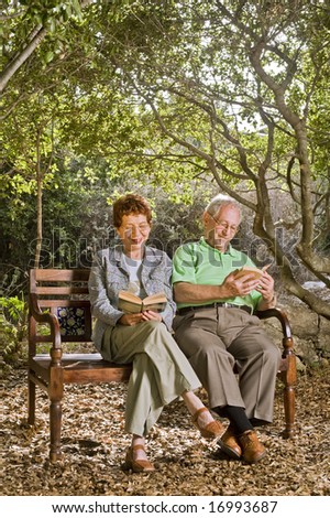 seniors couple sitting on a bench reading books in the park