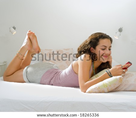 teenager girl lying in bed using her cell phone