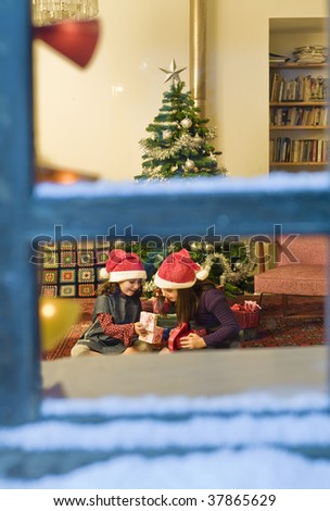 two little girls opening Christmas presents watched from a snowy window