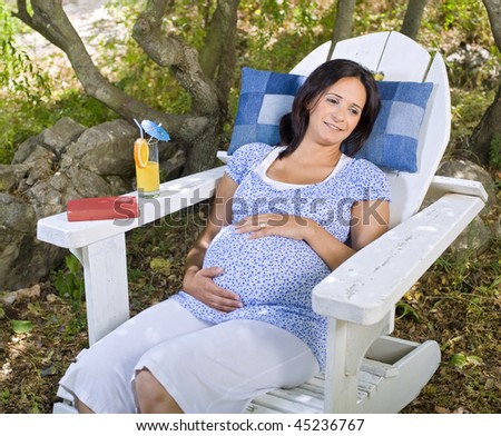 pregnant woman reading a book and drinking orange juice in an Adirondack chair