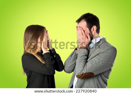 Couple covering their eyes over green background