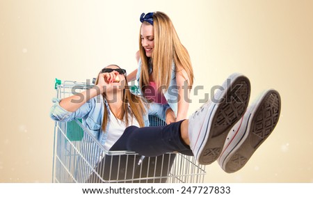 Girls playing with supermarket cart over ocher background