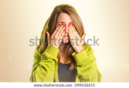young girl covering her eyes over ocher background