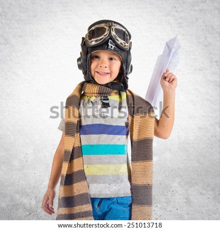 Kid dressed like pilot and playing with plane paper