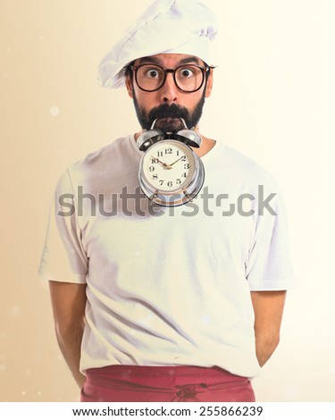 Crazy chef holding a clock over ocher background