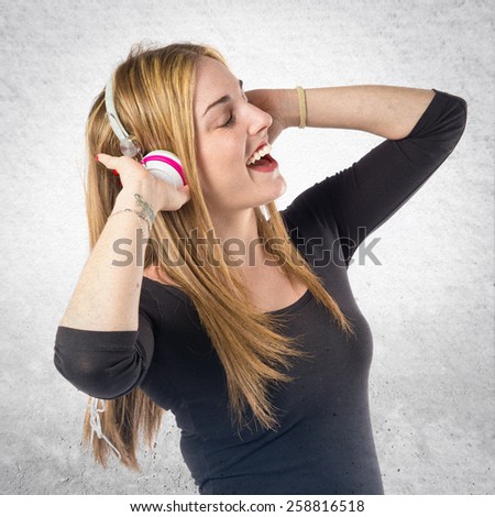 Young blonde girl listening music over textured background