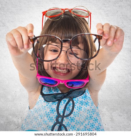 Girl wearing many sunglasses over grey background