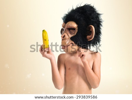 Child with monkey mask showing his banana over ocher background