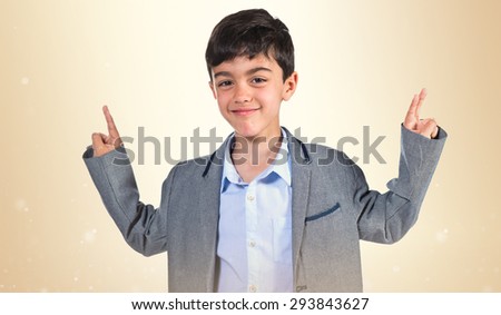 Child doing victory gesture over ocher background
