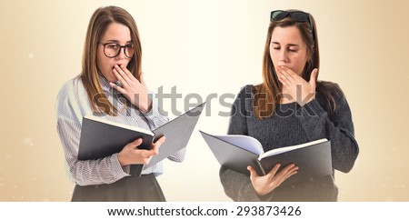 Surprised sisters reading book over ocher background