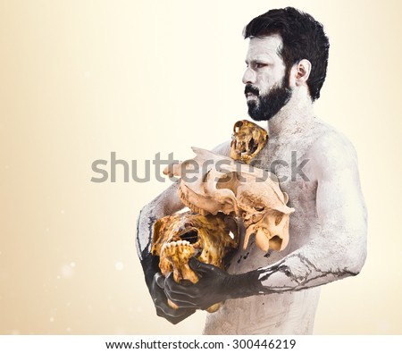 prehistoric man holding animal skulls over ocher background