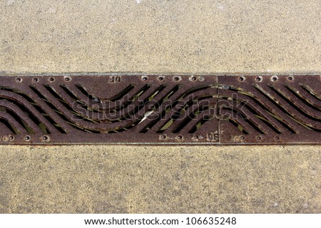 A elongated stylized floor drain made out of cast iron on the ground with patterns