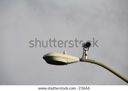 Traffic-control camera with streetlight, with a diffusely cloudy background.