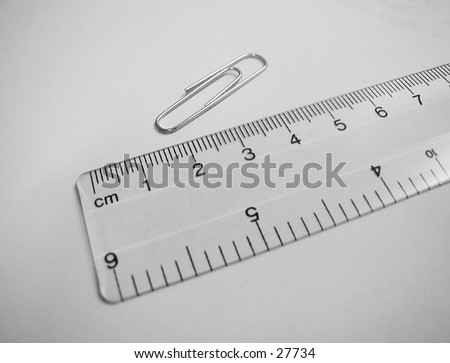 Transparent ruler and paper clip, metric scale showing, diagonal arrangement.