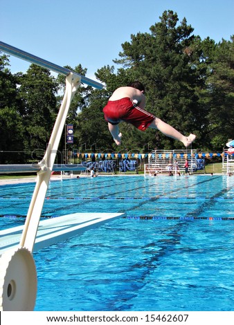 Boy doing a funny jump off the diving board at a public swimming pool.