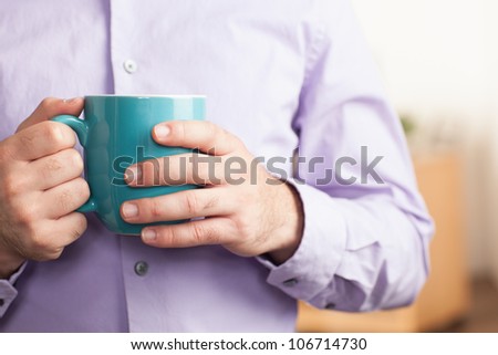 Detail of a man wearing a purple dress shirt holding a blue coffee mug.