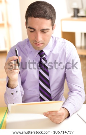 Good looking young business professional working on paper in a file folder in a business office. He\'s looking down and wearing a purple dress shirt & tie.