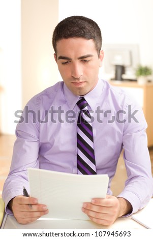 An attractive guy at work wearing a purple shirt and tie looking at paper with serious expression, holding paper in hands