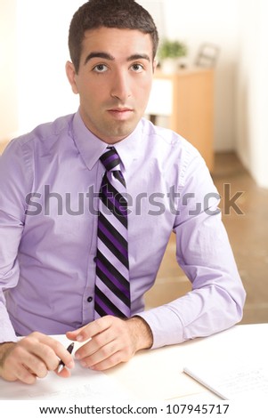 A handsome man at work with a surprised look on his face writing on paper wearing purple shirt and tie