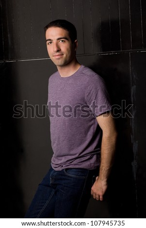 Good looking young guy leaning against black wall looking at camera