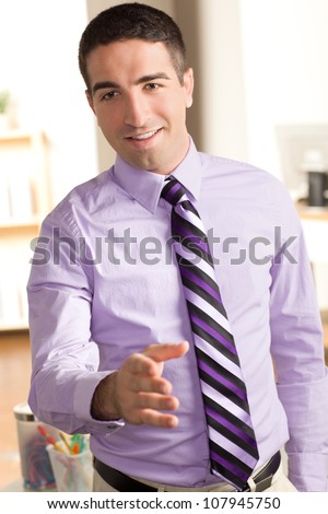 A cute business man extending his hand for a hand shake in an office setting with a smile on his face.