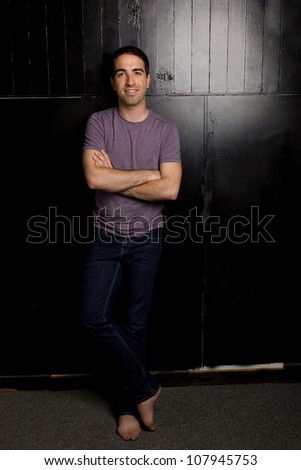 Good looking young guy leaning against black wall looking at camera