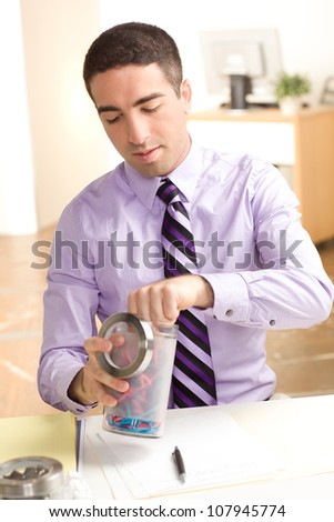 A man holding a bottle of rubber bands at work in an office setting wearing a purple shirt with tie
