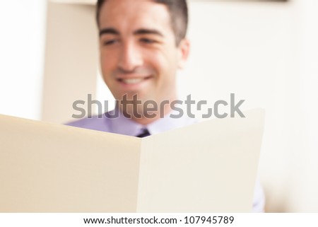 A close up of a cream folder that is in focus and a man smiling in the background. The man is out of focus