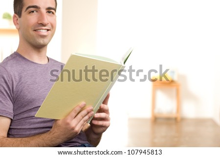 A handsome young man reading a book, smiling at camera wearing a lavender shirt. Includes copy space area.
