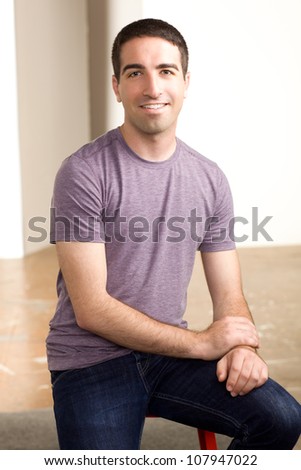 Good looking athletic guy sitting on a red stool wearing purple shirt and jeans