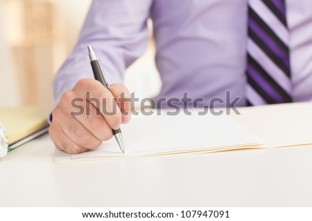 Detail shot of a business man writing on paper using pen wearing a purple shirt and tie