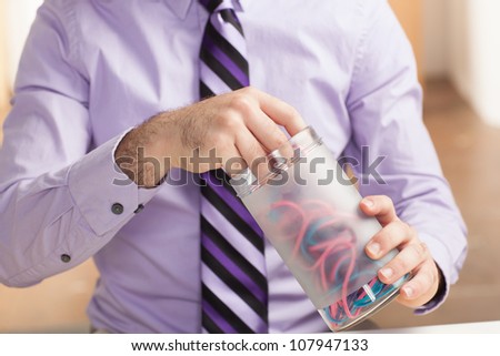 A detail shot of a man reaching into a glass container holding rubber bands. Shot includes his hands and part of his torso and a purple shirt and tie