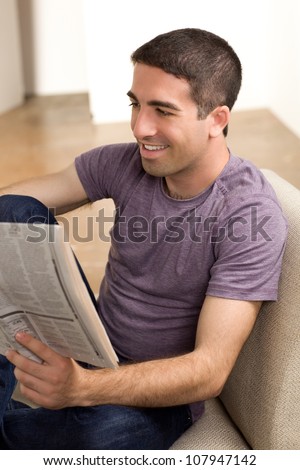 Good looking guy reading the newspaper sitting on a beige chair