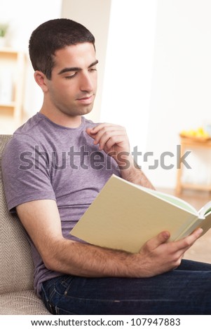 Attracting young man sitting in chair reading a book wearing purple shirt and jeans.