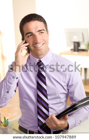 Handsome young business man on phone looking off holding a leather pad in an office setting