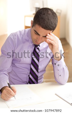 A good looking guy concentrating at work, looking down at paper, writing with pen, wearing a purple shirt and tie