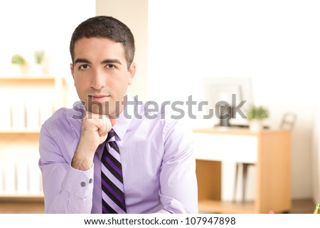 Good looking youthful fit business man looking at camera with straight face and chin leaning on fist in an office settting.