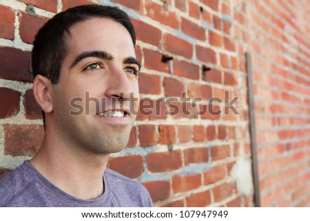 A portrait of cute man gazing off, leaning on brick wall with a purple shirt with copy space.