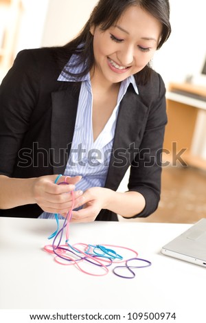 Cute Asian female having fun at work with rubber bands wearing a black suit and blue shirt.