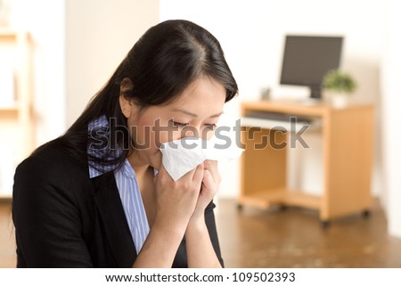 Cute Asian woman in an office setting with a cold wearing a black suit and blue shirt