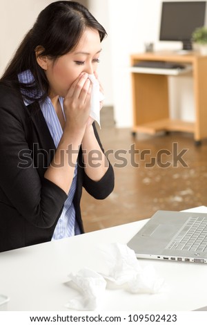 Cute Asian woman in an office setting with a cold wearing a black suit and blue shirt