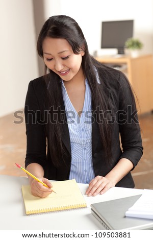 Attractive Asian woman at work in office setting with straight black hair wearing black suit and blue shirt