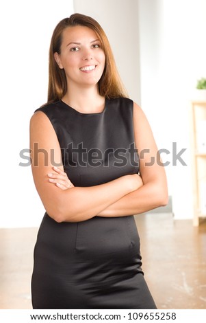 Beautiful Caucasian female at work wearing a sleeveless black dress with brunette hair.